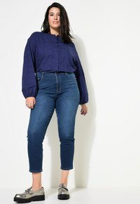 Marinblå knäppblus med strukturerat mönster, parat med högmidjade, åtsittande mörka jeans och silvriga loafers med tjock sula.