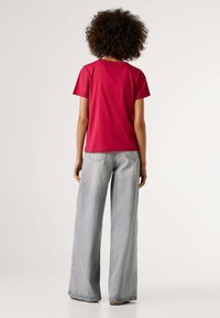 Rode katoenen t-shirt met korte mouwen en een ronde hals, gecombineerd met lichtgrijze jeans met wijde pijpen. Eenvoudig ontwerp, minimalistische stijl.