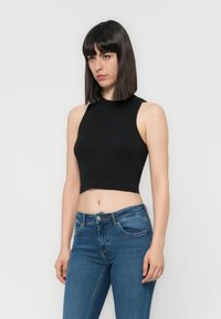 Svart, ermløs crop topp med høy hals-design. Kombinert med tettsittende blå jeans med lett stretch og klassisk fem-lomme design.