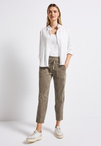 Chemise en lin blanche à boutons sur un débardeur blanc ; pantalon de jogging gris avec taille élastique et poches latérales ; baskets légères.