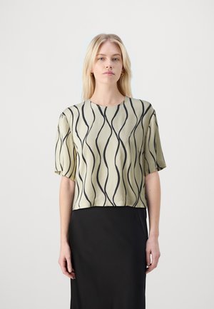 Short-sleeve top in pale green with black wave pattern. Smooth fabric, round neck, and cropped design. Paired with a black skirt.
