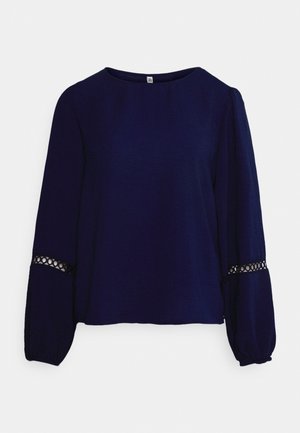 Námořnická modrá halenka s dlouhým rukávem a kulatým výstřihem, s texturovanou tkaninou a krajkovými detaily na manžetách. Volný střih.