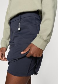 Calções azul-marinho feitos de um tecido elástico com uma textura suave, apresentando uma fenda lateral e um charme prateado pendurado na cintura.