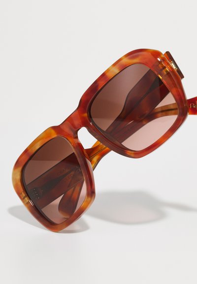 Lunettes de soleil écaille de tortue avec une monture carrée épaisse, des verres dégradés marron et des accents en métal doré. Fini lisse et brillant sur l'ensemble.