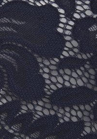 Tissu en maille bleu marine avec un motif floral comprenant des éléments en relief et en forme de vagues. La texture est complexe avec des sections en tissage ouvert et des motifs pleins.