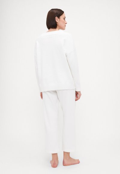 White sweater with a textured finish, featuring dropped shoulders and a wide fit. Paired with white, cropped pants. Barefoot model.