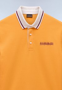 Gul polo skjorte lavet af struktureret stof, med en hvid krave med maroon striber og et lilla mærke-logo på venstre side.