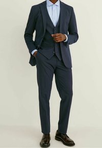 Marinblå tre-delad kostym med subtila randningar, i kombination med en ljusblå skjorta. Har en skräddarsydd passform och stiliga bruna skor.