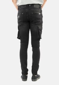 Černé cargo kalhoty slim fit, s několika kapsami, zipovými detaily na stehnech, denimovým materiálem a mírně ošuntělou texturou.