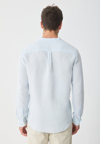Light blue long-sleeve shirt made of linen, featuring a round collar, back pleat, and buttoned cuffs. Soft texture and curved hem.