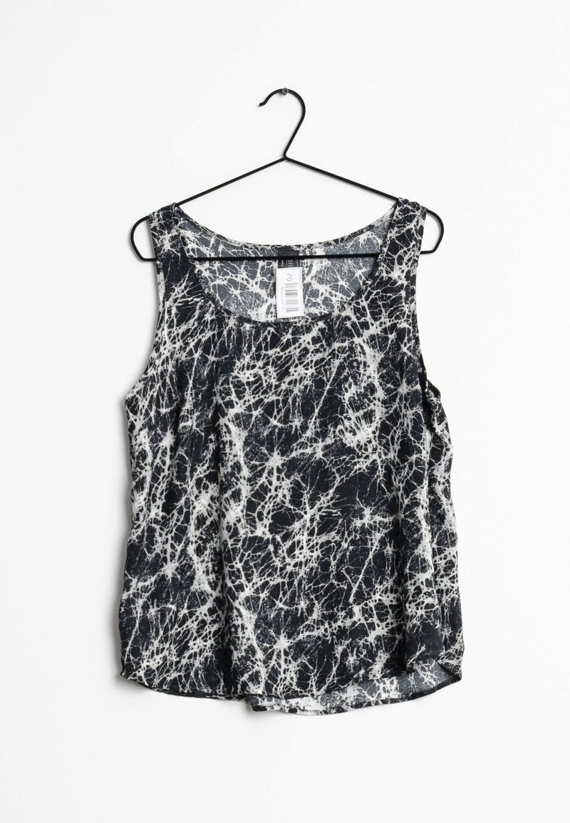 Haut sans manches noir et blanc avec motif abstrait éclaboussé suspendu à un cintre en fil métallique noir sur fond blanc.
