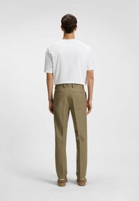 Vêtements pour hommes : chemise blanche à manches courtes, pantalon kaki, tissu texturé, deux poches arrière, accompagnée de chaussures marron, montrée de dos.