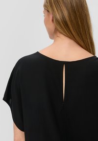 Top negro con escote redondeado y espalda abierta con una pequeña abertura. Tela suave y ligera con un corte holgado y mangas cortas.