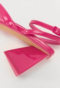 Rosa høyhælte sandaler med en glanset finish, med tynne stroppbidrag og en tykk geometrisk hæl for et moderne design.