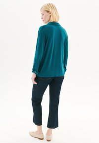 Takkirakennettu pitkähihaisen puseron kanssa, jossa on kaulukset ja nappikuosia, yhdistetty tummansiniset capri-housut ja vaaleat liuku kengät.