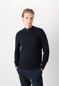 Marinblå zip-tröja med rund hals tillverkad av mjukt stickat tyg, med långa ärmar samt ribbade detaljer vid krage och ärmslut; diskret logotyp i matchande färg.