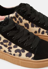 Sneakers in camoscio nero e stampa animale presentano un tessuto testurizzato, lacci neri spessi, suole in gomma e una suola color beige.