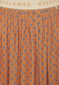 Orange blommig kjol med små lila och vita blommönster, rynkat tyg och en beige midja tryckt med "WILDFLOWER" i orangea bokstäver.