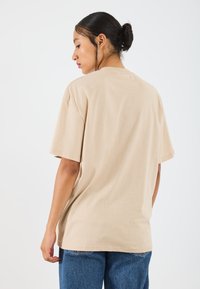 Beige cotton t-shirt with short sleeves, relaxed fit, and a round neckline. Smooth texture, featuring no visible patterns or accents.
