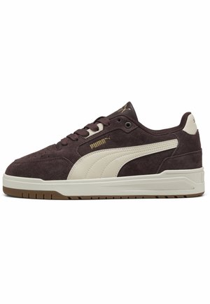 Ciemnobrązowy zamszowy sneaker Puma z białym paskiem po boku, gumową podeszwą, sznurowadłami i złotym logo Puma po boku i na języku, widziany z lewej strony.