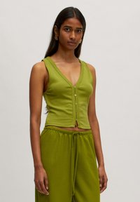 Grüner ärmelloser Oberteil mit tiefem V-Ausschnitt, der fünf kleine Knöpfe auf der Vorderseite hat und einen cropped Schnitt aufweist, aus weichem Material gefertigt.