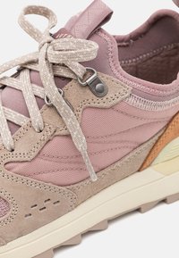 Ljusrosa träningssko med blandade material, inklusive mocka och nät, texturerade snören och en off-white sula. Syt detaljer synliga.