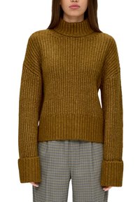 Gestrickter Rollkragenpullover in senfgelb mit gerippten Bündchen und Saum. Weicher, strukturierter Stoff, lockere Passform, kombiniert mit karierten Hosen.