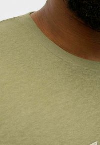 Olivgrünes T-Shirt mit rundem Ausschnitt, aus weichem, strukturiertem Stoff, mit einem subtilen Muster entlang des Saums.