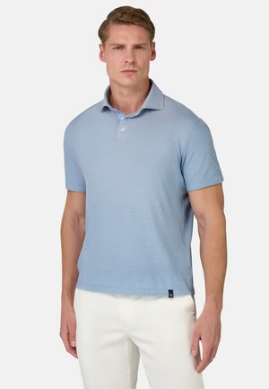 Himmelblaues Poloshirt mit kurzem Kragen, Knöpfen und strukturiertem Stoff, kombiniert mit weißen Hosen. Besitzt ein Logotag am Saum.