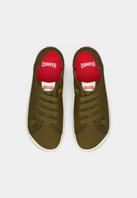 Baskets en toile vert olive avec six œillets, semelles en caoutchouc blanches et semelles intérieures rouges affichant le logo "CAMPER". Présente une tige texturée et des accents latéraux.