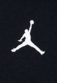 Hvit brodert Jumpman-logo på en svart stoffbakgrunn, som viser en spiller i luften med en basketball.