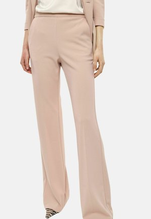 Donna che indossa pantaloni rosa cipria a vita alta e gamba larga abbinati a un blazer coordinato e scarpe con punta a stampa animale.