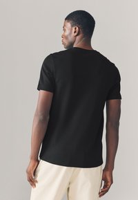 Black short-sleeve t-shirt made of cotton, featuring a round neckline and a relaxed fit, worn with light-colored pants.