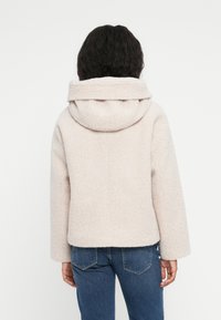 Lyserød hættejakke med en tekstureret finish, brede ærmer og en let cropped pasform. Minimalistisk design, ingen synlige lukninger eller detaljer.