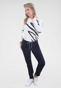 Biely dlhý rukáv s čiernymi abstraktnými pruhmi, skombinovaný s námorníckymi jogger nohavicami a bielymi teniskami. Elegantný dizajn s voľným strihom.