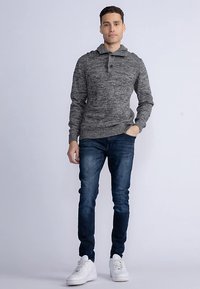 Grauer Strickpullover mit Kragen und zwei Knöpfen, kombiniert mit dunkelblauer Jeans und weißen Turnschuhen. Der Pullover hat ein strukturiertes Design.