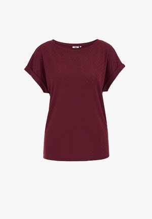 Sarkana īsroku blūze ar teksturētu zivju kaulu rakstu, apaļu izgriezumu un brīvu piegriezumu. Audums šķiet mīksts un viegls.