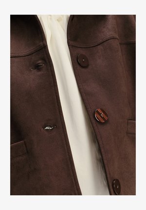 Giacca in suede marrone con due tasche frontali, due bottoni marroni, cuciture visibili e uno strato interno bianco.