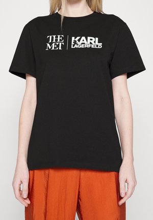 Musta puuvillainen t-paita, jossa valkoiset "THE MET"- ja "KARL LAGERFELD" -logot. Pyöreä kaula-aukko ja lyhyet hihat. Yhdistetty oransseihin teksturoiduihin housuihin.
