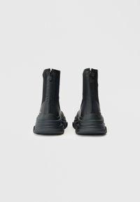 Zwarte hoge laarzen met een gladde synthetische bovenkant, ritssluiting aan de achterkant en een stevige gestructureerde zool. Minimalistisch ontwerp, slanke silhouet.