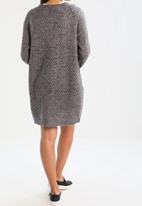 Pitkä harmaa neulemekko, jossa on tekstuuri kuvio, pyöreä pääntie ja väljä istuvuus, yhdistettynä mustiin liukusilkkikenkiin.