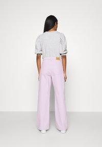 Jeans a gamba larga di un leggero viola e una maglietta grigia con maniche a palloncino; texture in denim e evidente dettaglio dell'etichetta sul retro.