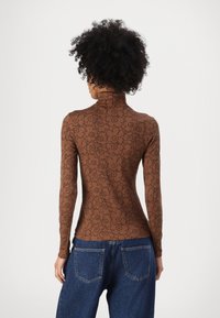 Brauner Langarmoberteil mit hohem Kragen, in Schwarz mit floralem Muster. Kombiniert mit blauen Jeans, die eine figurbetonte Silhouette zeigen.