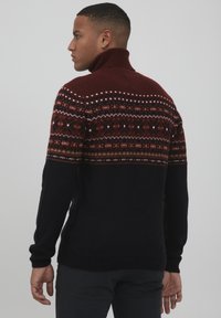 Strickpullover mit einem burgunderrot und marineblauen Farbschema, hohem Kragen und geometrischen Mustern in Orange und Creme im oberen Bereich.