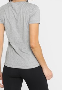 Camiseta gris de manga corta con cuello redondo, corte ajustado y textura suave; combinada con leggings negros, mostrando un conjunto casual.
