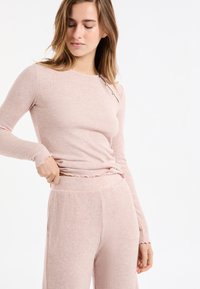 Jasnoróżowa prążkowana bluzka z długim rękawem, okrągłym dekoltem i guzikiem po boku; zestawiona z dopasowanymi prążkowanymi spodniami o luźnym kroju.