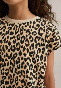 Leopardų raštas su trumpomis rankovėmis marškinėliai su apvaliu iškirpimu, pagaminti iš minkštos medvilnės. Fonas – smėlinis, su juodais taškeliais ir raištiniu apykaklės kraštu.