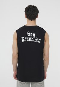 Maglietta nera senza maniche con scritta grafica bianca: "San Francisco, le cose belle richiedono tempo" sulla schiena. Materiale in cotone morbido.