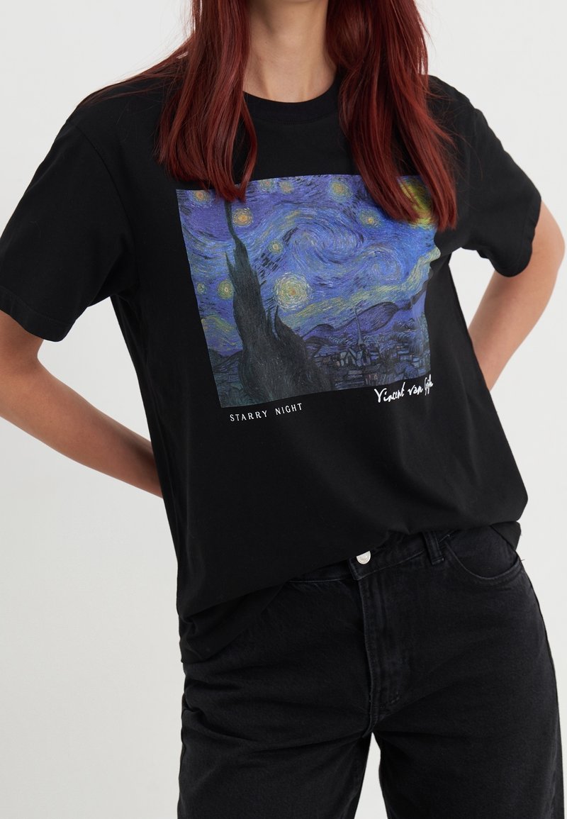 Camiseta negra con una impresión colorida de "Noche estrellada" de Vincent van Gogh, con un cuello redondo amplio y mangas cortas.