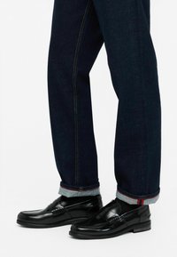 Zwarte leren loafers met een gepolijste afwerking, gecombineerd met donkere denimbroeken met een omgeslagen zoom en contrasterende rode stiksel.